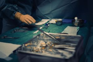 Surgical instruments arranged on a green operating table with a gloved hand reaching for them.
